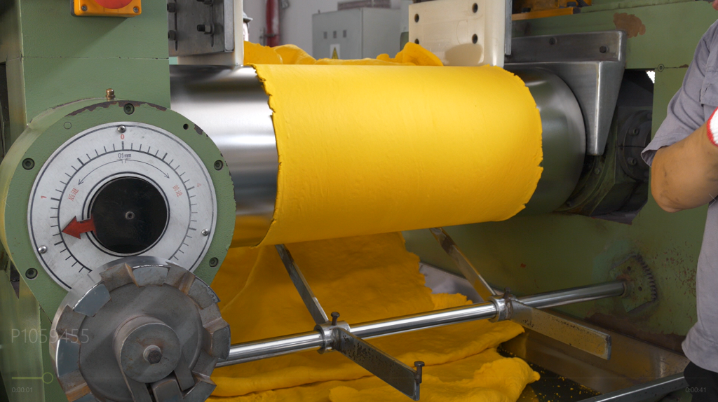 Inside view of a rubber compound mixer, with FKM material undergoing high-shear blending with curatives and additives. Dense, homogeneous FKM compound being discharged from the mixer onto a mill, demonstrating its uniform texture and quality.